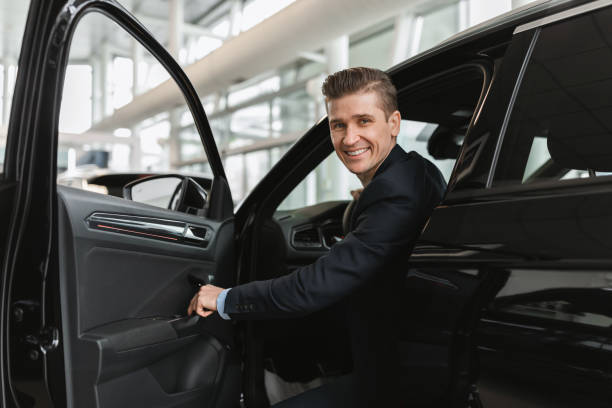 istock Successful millennial car salesman sitting inside auto salon, looking at camera through open door in modern dealership 1477805742