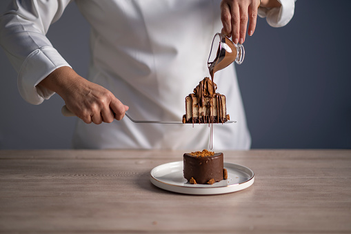 Female chef pouring chocolate sauce on cake.