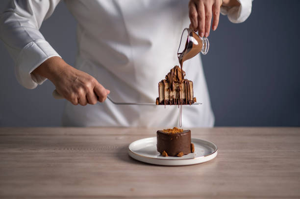 Female chef pouring chocolate sauce on cake stock photo