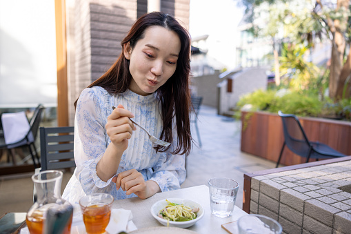 Young woman eating spaghetti genovese at outdoor cafe