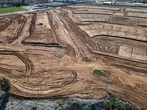 An aerial view of a construction site featuring a large dirt field, divided up into multiple sections