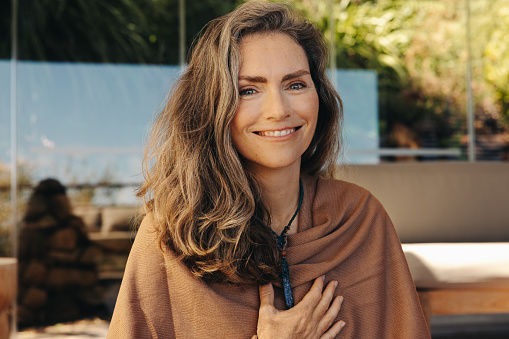 Senior woman smiling at the camera while wearing a crystal necklace. Mature woman meditating and practicing crystal healing at home. Happy senior woman following a holistic lifestyle.