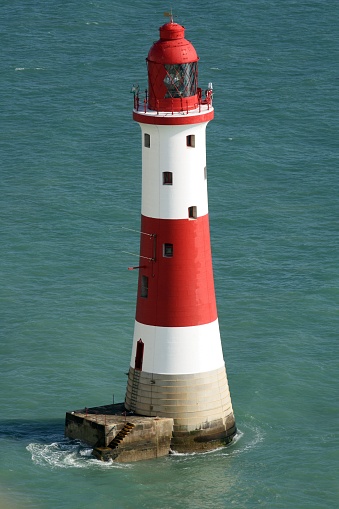 A picturesque red and white lighthouse situated among the waves of a tranquil coastal scene