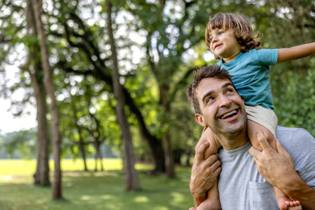 Happy father carrying his son on his shoulders at the park Happy Brazilian father carrying his son on his shoulders while having fun at the park father holding son stock pictures, royalty-free photos & images