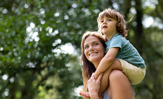 Happy Brazilian mother carrying her son on her shoulders at the park and smiling - family lifestyle concepts