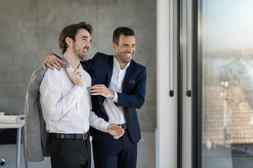 Two successful male entrepreneurs looking through window in the office and laughing