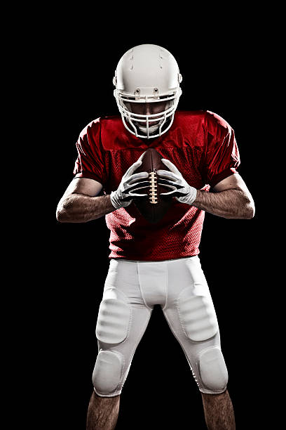 A football player ready to play Football player with a ball in the hands, looking to the ball. Photo made in studio with black background and hard light. american football player studio stock pictures, royalty-free photos & images