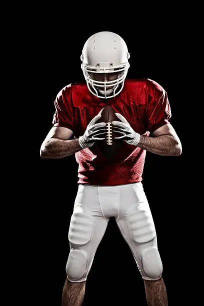 Football player with a ball in the hands, looking to the ball. Photo made in studio with black background and hard light.