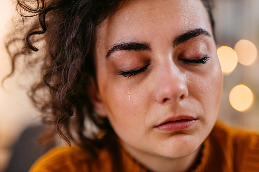 Close-up of a sad young woman crying at night at home.