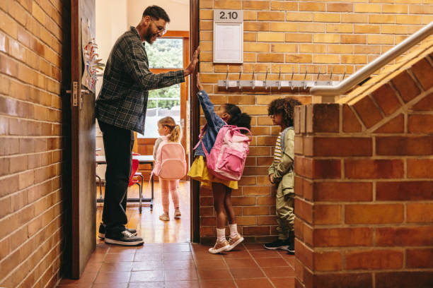 insegnante di scuola elementare che saluta i suoi studenti alla porta. insegnante maschio che accoglie la sua classe con un cinque alto - teacher foto e immagini stock