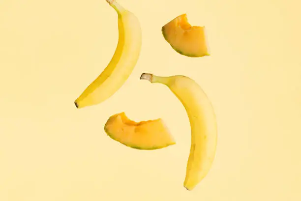 Bananas and melon slices hover over isolated pastel yellow background. Minimal creative concept of tropical summer fruit. The idea of raw food diet rich in potassium.