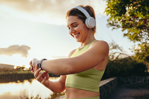 Sports woman choosing a fitness playlist using a smartwatch outdoors. Happy woman going for a morning run with headphones. Woman using technology for a workout.