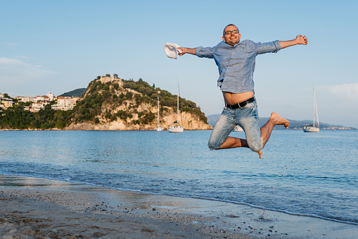 Handsome young man jumping of joy on the beach in Parga, Greece.