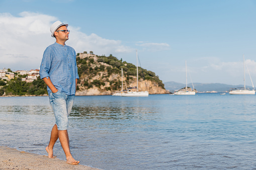 Handsome young man walking barefoot on the beach in Parga, Greece.