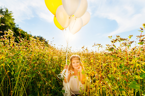 Stylish girl 4-5 years old holding a balloon in a trendy white dress on the meadow. Birthday.