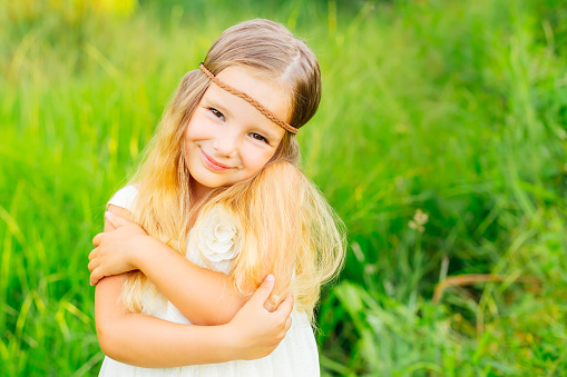 Cute little girl outdoors with curly white hair on a background of green grass.