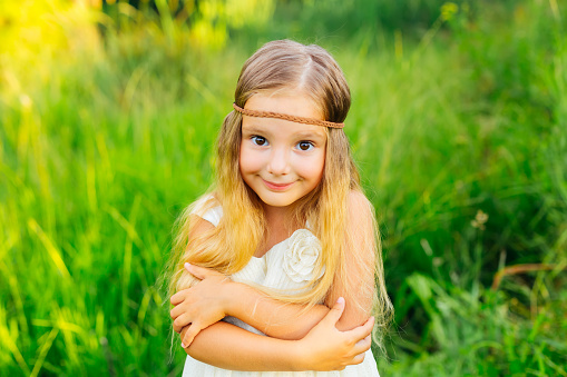 Smiling girl on a green meadow, a small child hugs herself, wearing a white dress and a bandage on her forehead.