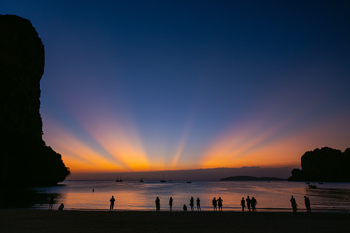 Crowd of people standing on the beach and  looking at vibrant unusual sunset over the sea