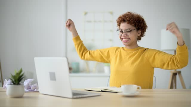 Woman looked at laptop screen at home office, read or saw good news and began to wave hands, laugh and toothy smile with happiness. Promotion at work, career success, finish doing freelance work.