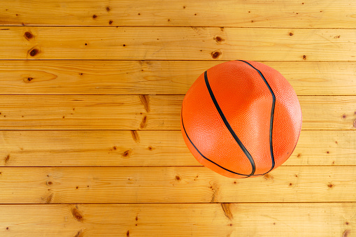 A basketball that is bumpy due to leaks and no gas inside put on wooden floor isolated on white background.