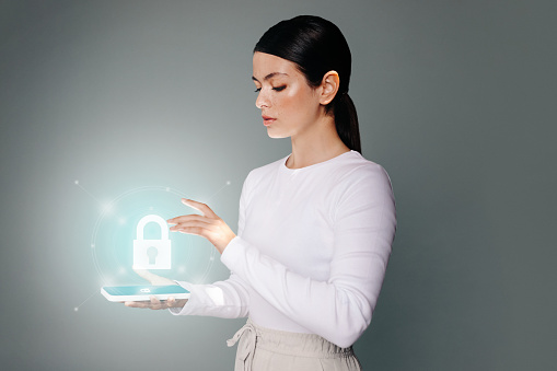 Woman unlocking her smartphone using fingerprint authentication in a studio. Young woman in her 20's gaining access to her mobile device using a biometric identification software.