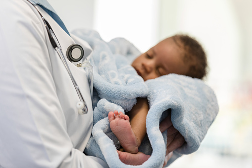 The focus of the photo is on the newborn baby boy's cute tiny feet as he sleeps trustingly in the unrecognizable doctor's arms.