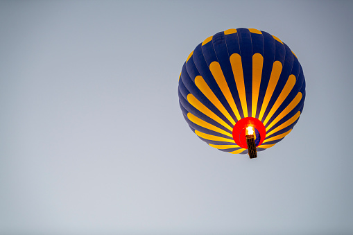 Closeup view of colorful hot air balloon on blue sky background at sunrise. The balloon is flying over Goreme Historical National Park, Cappadocia, Turkey. Cappadocia is a popular tourist destination.