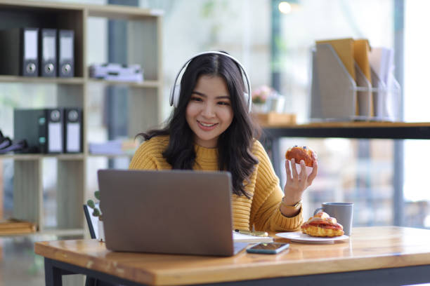 istock Attractive beautiful Asian woman casually working on laptop in office and having snacks. 1477834591