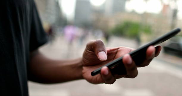 istock Close-up black man hand holding cellphone device in street 1477836174