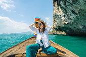 Cheerful woman traveling with Thai taxi boat and photographing with point and shoot camera