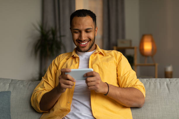 istock Happy young black man using smartphone, chatting online, sitting on couch at home 1477839578