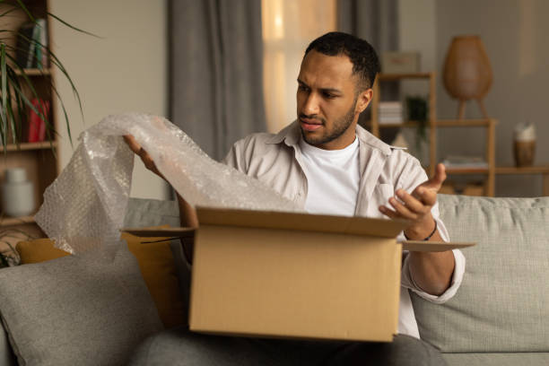 istock Dissatisfied black male customer opening box from online store, taking out packaging, unhappy with received item at home 1477840829