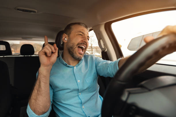 Happy man in earphones enjoying music driving luxury car Favorite Song. Portrait of excited playful man in wireless earphones driving luxury car, dancing to music and singing, resting on weekend going on summer vacation, windshield view singing stock pictures, royalty-free photos & images