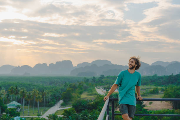 homme aux cheveux bouclés regardant la vue panoramique sur la jungle depuis le toit - phuket province thailand tourist asia photos et images de collection