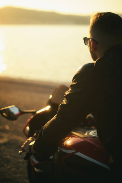 夕暮れ時に赤いレースバイクにサングラスをかけた若い男のバックビュー - motorsprot ストックフォトと画像
