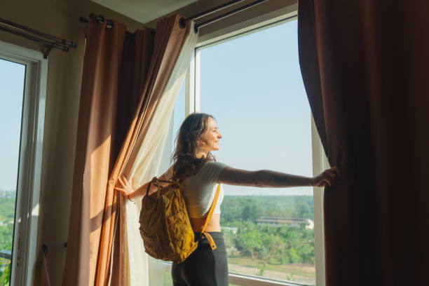 Woman walking in to her room in hotel and looking through window on the view of jungles Young Caucasian woman with backpack walking in to her room in hotel and looking through window on the view of jungles luxury-villa-view stock pictures, royalty-free photos & images