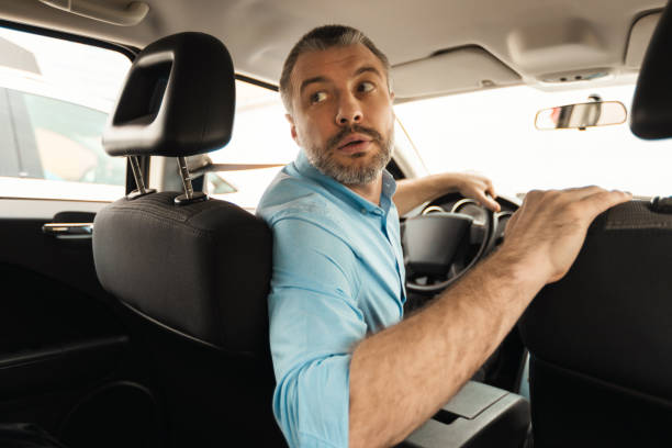 Middle Aged Male Driver Driving Car In Reverse Looking Back