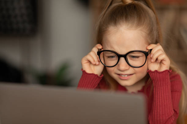 niña entrecerrando los ojos usando una computadora portátil con gafas en casa - entrecerrar los ojos fotografías e imágenes de stock