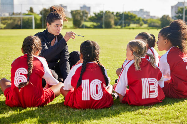 istock Coaching, exercise or coach with children for soccer strategy, training and team goals in Canada. Team building, teamwork and woman planning group of girl on football field for game, match or workout 1477844831