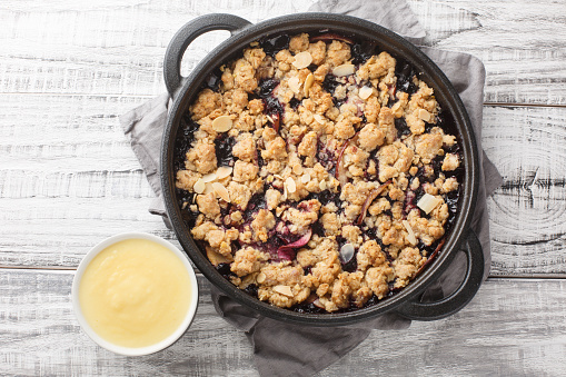 Berry fruit crumble baked with apples and blueberries served with vanilla sauce close-up in a pan on the table. Horizontal top view from above