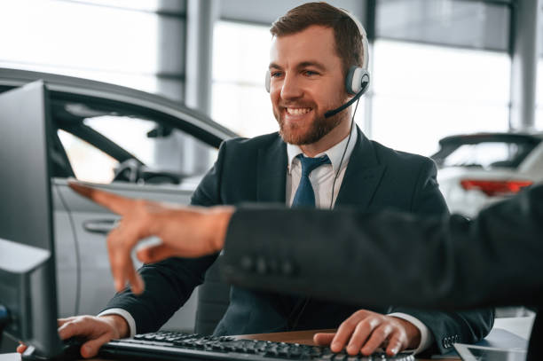 sitting in the headphones, using pc. two businessmen are working together in the car showroom - car dealership audio imagens e fotografias de stock