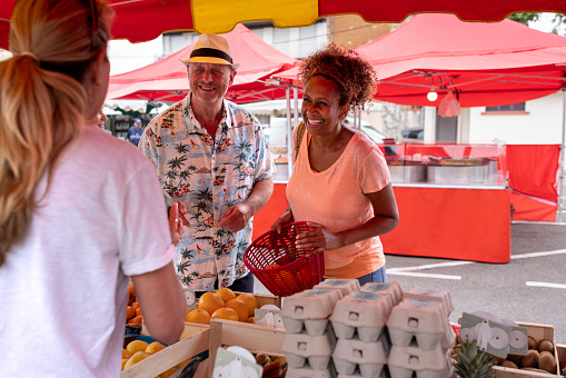 An over the shoulder view of a market trader speaking to a senior couple who are enjoying a getaway to Toulouse in the South of France. The market stall holder is selling locally sourced products.