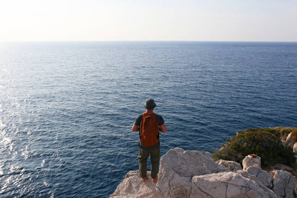 back view of a man at the edge of the cliff. - hiking coastline waters edge sunny imagens e fotografias de stock