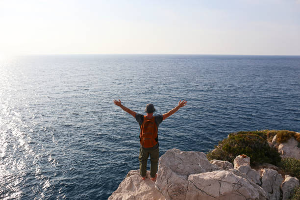 back view of a man at the edge of the cliff. - hiking coastline waters edge sunny imagens e fotografias de stock