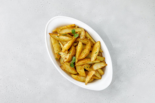 Baked potato wedges in white baking dish. Roasted potatoes with herbs and spices. Top view with copy space.