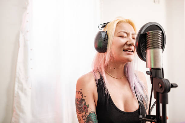 Female Korean Musician practising at home recording studio. She is dressed in casual black dress .  Interior of home recording studio.