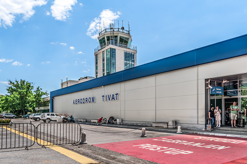 Tivat, Montenegro - June 16, 2021: Tivat airport building with a title sign on the wall - outside view. Passengers-travelers stand at the entrance to a modern building with the airport tower