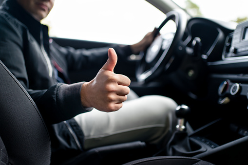 Happy driver in car, thumbs up. Man driving. Smiling positive new vehicle buyer and owner. Good customer service in taxi, dealership, insurance, inspection or maintenance business.