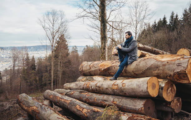 Caucasian white man in heavy dressing watching over Zurich from a height in Uetliberg while sitting on logs in an overcast winter day