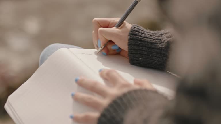 close up hands woman writing in diary journal teenage girl expressing lonely thoughts on seaside beach